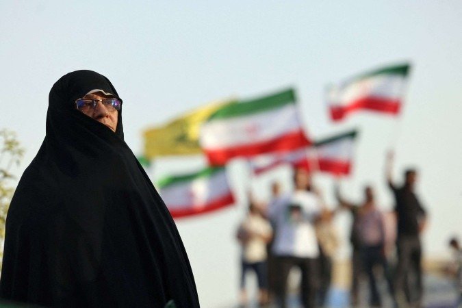 Iraniana diante de grupo celebrando trégua com bandeiras do país, na Praça Enghlab, em Teerã: mortos passam de 600 nos 12 dias de conflito -  (crédito: Atta Kenare/AFP)