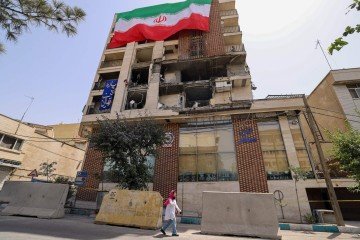 Iraniana caminha diante de prédio atingiddo por bombardeio israelense, em Teerã: fachada com a bandeira do país - (crédito: Atta Kenare/AFP) Iraniana caminha diante de prédio atingiddo por bombardeio israelense, em Teerã: fachada com a bandeira do país - (crédito: Atta Kenare/AFP)