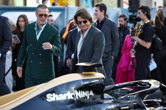 O ator e produtor americano Brad Pitt (E) conversa com o ator americano Tom Cruise (C) enquanto admiram o carro na chegada para a estreia europeia do filme F1 -  (crédito:  HENRY NICHOLLS / AFP)