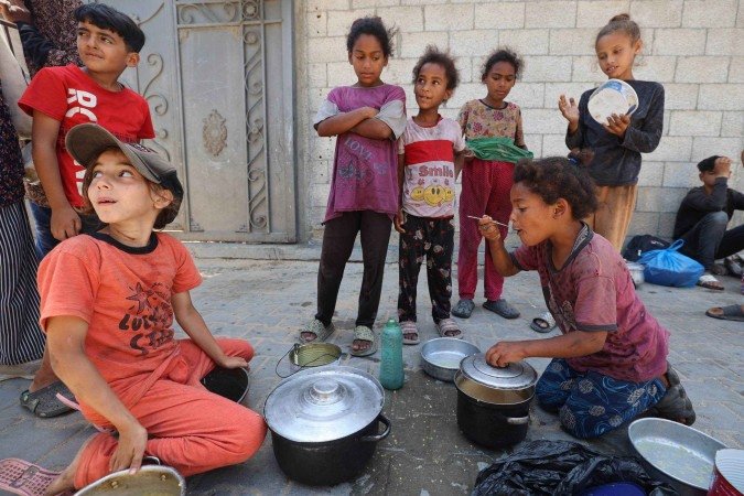 Crianças palestinas comem após ganharem uma refeição quente em um ponto para recebimento de alimentos em Nuseirat - (crédito: AFP) Crianças palestinas comem após ganharem uma refeição quente em um ponto para recebimento de alimentos em Nuseirat - (crédito: AFP)