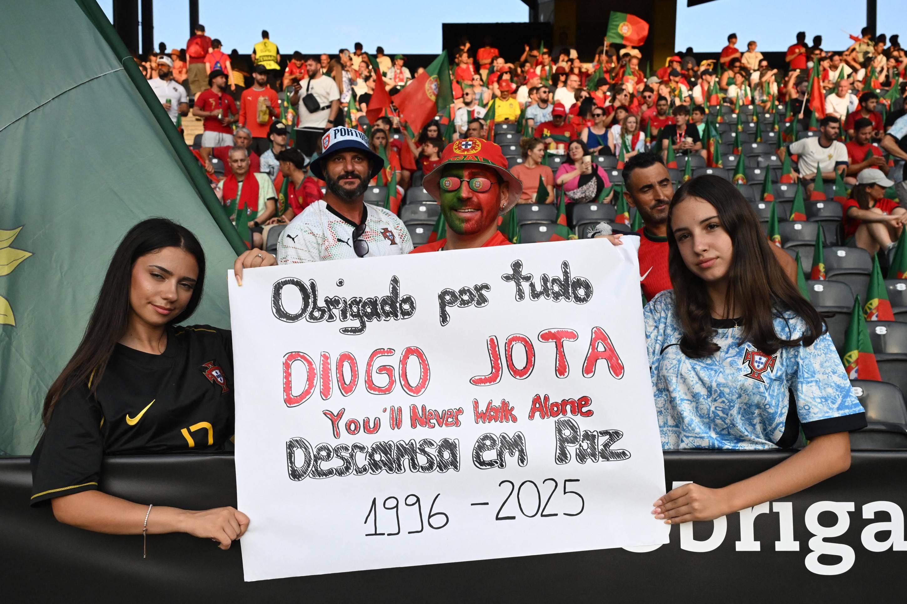 Torcedores seguram cartazes enquanto prestam homenagem ao atacante português do Liverpool, Diogo Jota. (Photo by Miguel MEDINA / AFP)       