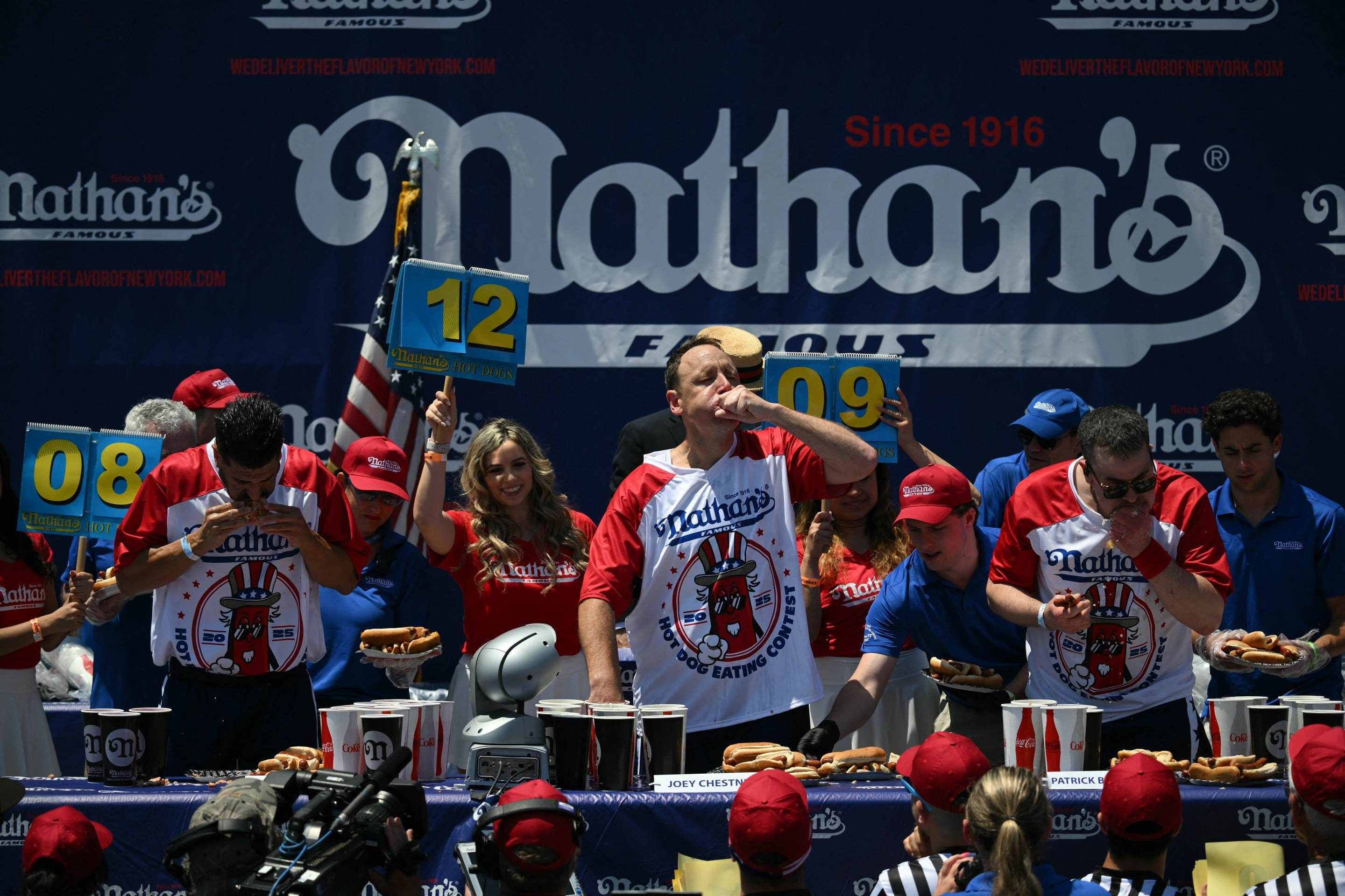 Patrick Bertoletti (à direita) comemora após terminar em 2º lugar no título masculino durante a competição de comer cachorro-quente Concurso Anual de Comer Cachorro-Quente do Nathans de 2025 em Coney Island, no bairro do Brooklyn, em Nova York, em 4 de julho de 2025   