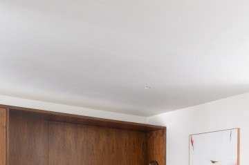 No projeto de Marcella Schiavoni, o chão e parte da parede em marrom escuro contrasta com mobiliário mais claro e um ponto colorido, no caso, o quadro