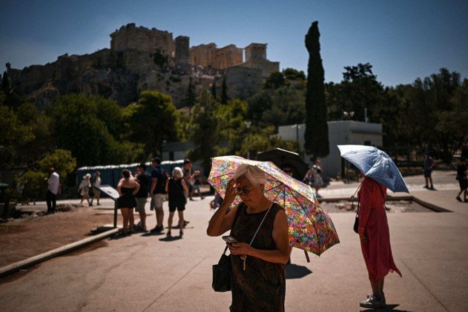 Turistas seguram guarda-chuvas enquanto caminham em frente à Acrópole, em Atenas, em 8 de julho de 2025       -  (crédito: Aris MESSINIS/AFP)