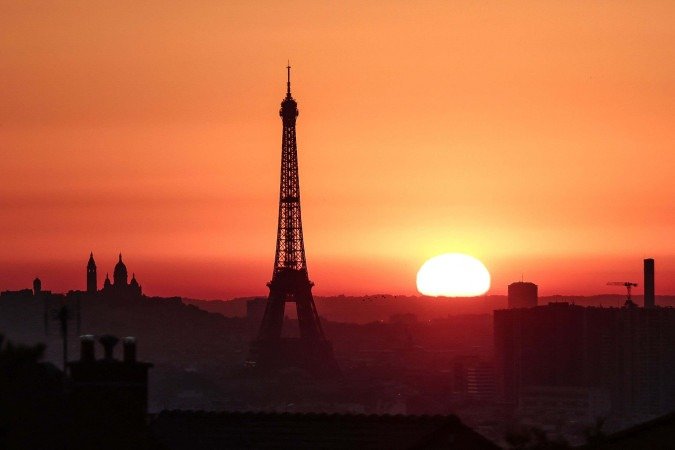 O sol nasce perto da Torre Eiffel e da Basílica do Sagrado Coração, no topo da colina de Montmartre       -  (crédito: Thibaud MORITZ/AFP)