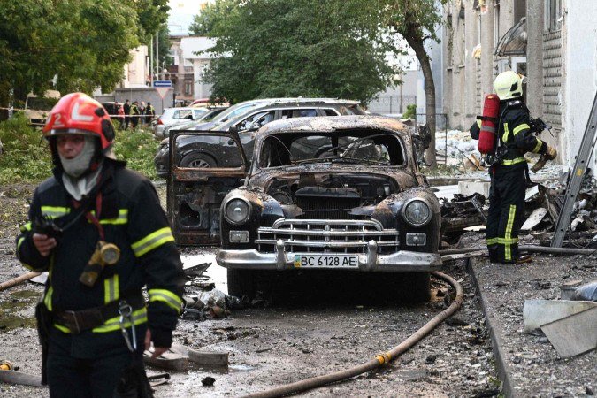  Firefighters stand next to a burnt-out car following mass Russian drone and missile strikes in the western Ukrainian city of Lviv on July 12, 2025, amid the Russian invasion of Ukraine. (Photo by YURIY DYACHYSHYN / AFP)       