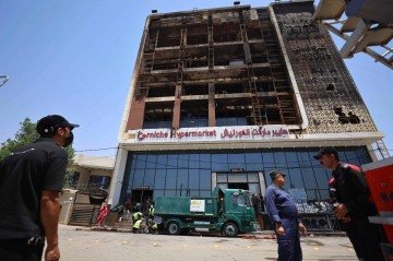 Uma operação de limpeza começa do lado de fora do prédio carbonizado em 17 de julho de 2025, após um incêndio ter atingido o recém-inaugurado Hyper Mall durante a noite    -  (crédito: AHMAD AL-RUBAYE/AFP)