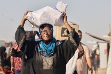 Mulher carrega saco de farinha perto de um centro de distribuição de ajuda, na região de Rafah, no sul
