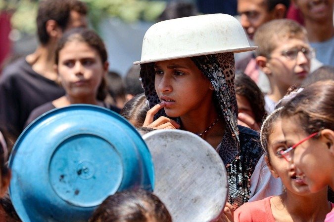 Garota cobre a cabeça com bacia para se proteger do sol, em centro de distribuição de comida, na Cidade de Gaza 