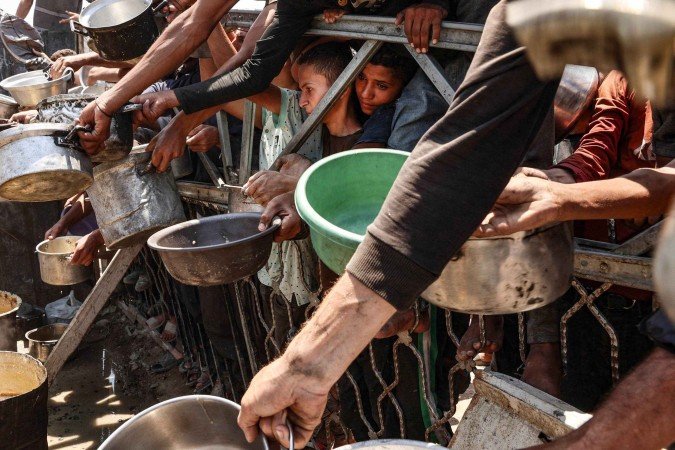 Com panelas e vasilhas nas mãos, palestinos imprensados em grade aguardam a entrega de comida 