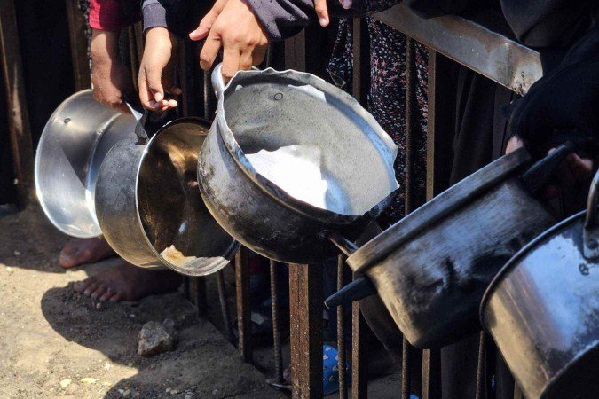 Palestinos carregam sacos de farinha de caminhões de ajuda humanitária que chegam do cruzamento de fronteira em Zikim, no norte da Faixa de Gaza -  (crédito: Majdi Fathi/NurPhoto/Getty Images)