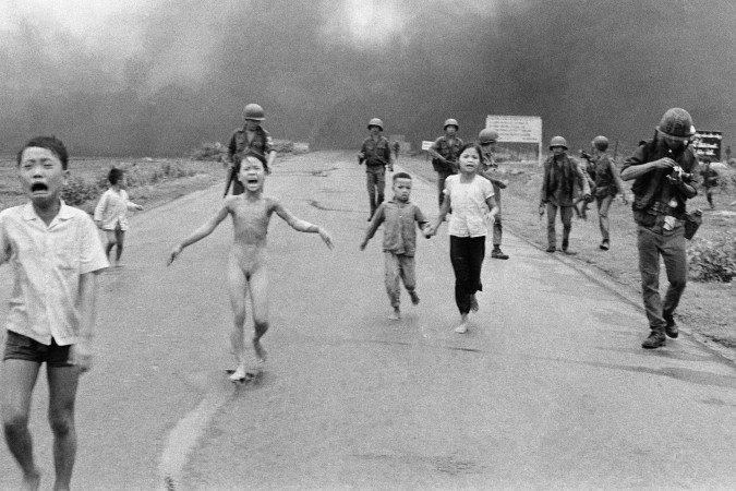 Em outra imagem do mesmo momento, Nguyen Thanh Nghe pode ser visto segurando uma câmera parecida com uma Pentax (esquerda); à direita, uma figura usando equipamento de proteção que poderia ser Nick Ut pode ser vista no vídeo (direita). - (crédito: Getty Images) Em outra imagem do mesmo momento, Nguyen Thanh Nghe pode ser visto segurando uma câmera parecida com uma Pentax (esquerda); à direita, uma figura usando equipamento de proteção que poderia ser Nick Ut pode ser vista no vídeo (direita). - (crédito: Getty Images)