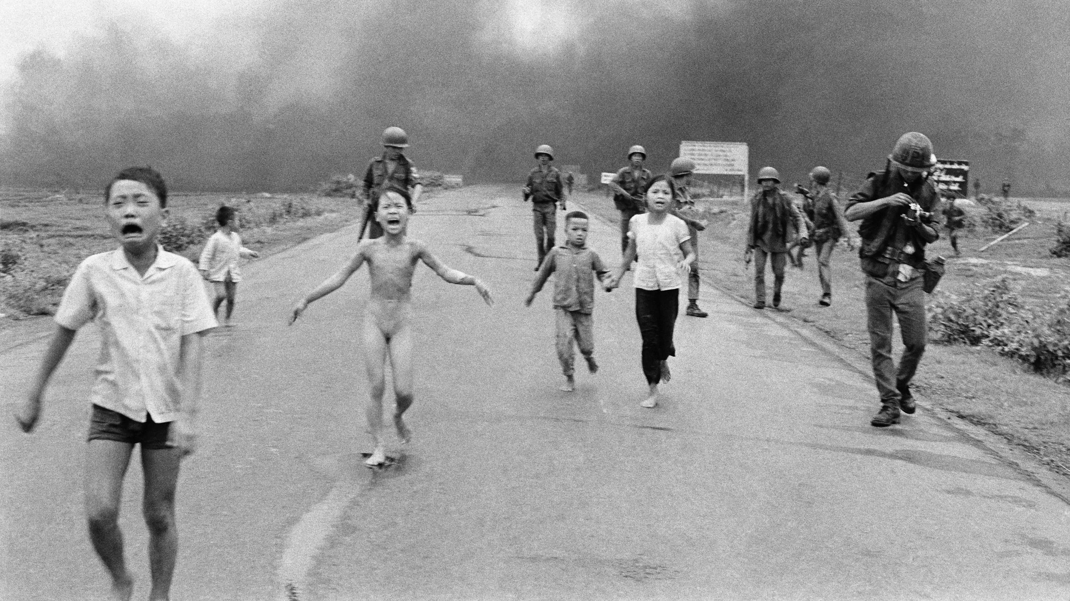 Em outra imagem do mesmo momento, Nguyen Thanh Nghe pode ser visto segurando uma câmera parecida com uma Pentax (esquerda); à direita, uma figura usando equipamento de proteção que poderia ser Nick Ut pode ser vista no vídeo (direita). -  (crédito: Getty Images)