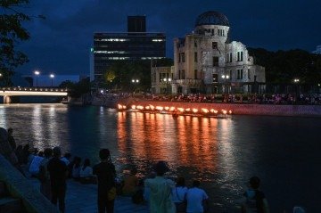Pessoas assistem enquanto pequenas fogueiras são acesas ao longo do Rio Motoyasu em frente ao Domo da Bomba Atômica durante uma cerimônia em memória das vítimas na véspera do 80º aniversário do primeiro ataque com bomba atômica do mundo, na cidade de Hiroshima, em 5 de agosto de 2025       -  (crédito: RICHARD A. BROOKS/AFP)