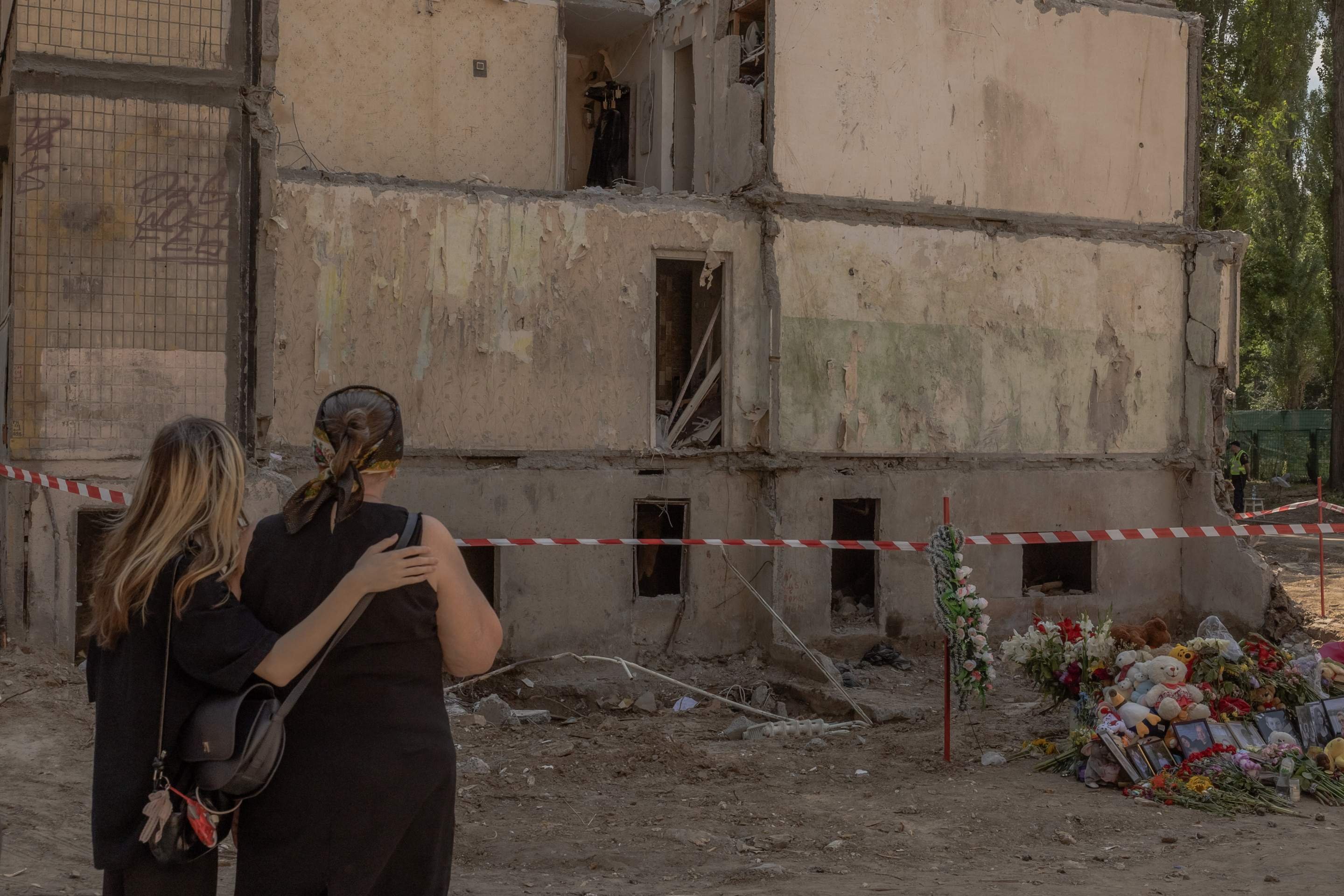 Mulheres observam flores, brinquedos e fotos em memorial a vítimas de bombardeio russo a prédio de nove andares, em Kiev Mulheres observam flores, brinquedos e fotos em memorial a vítimas de bombardeio russo a prédio de nove andares, em Kiev
