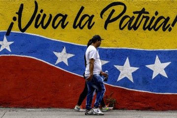 Morador de Caracas passa por mural com as cores da bandeira venezuelana e a frase: 