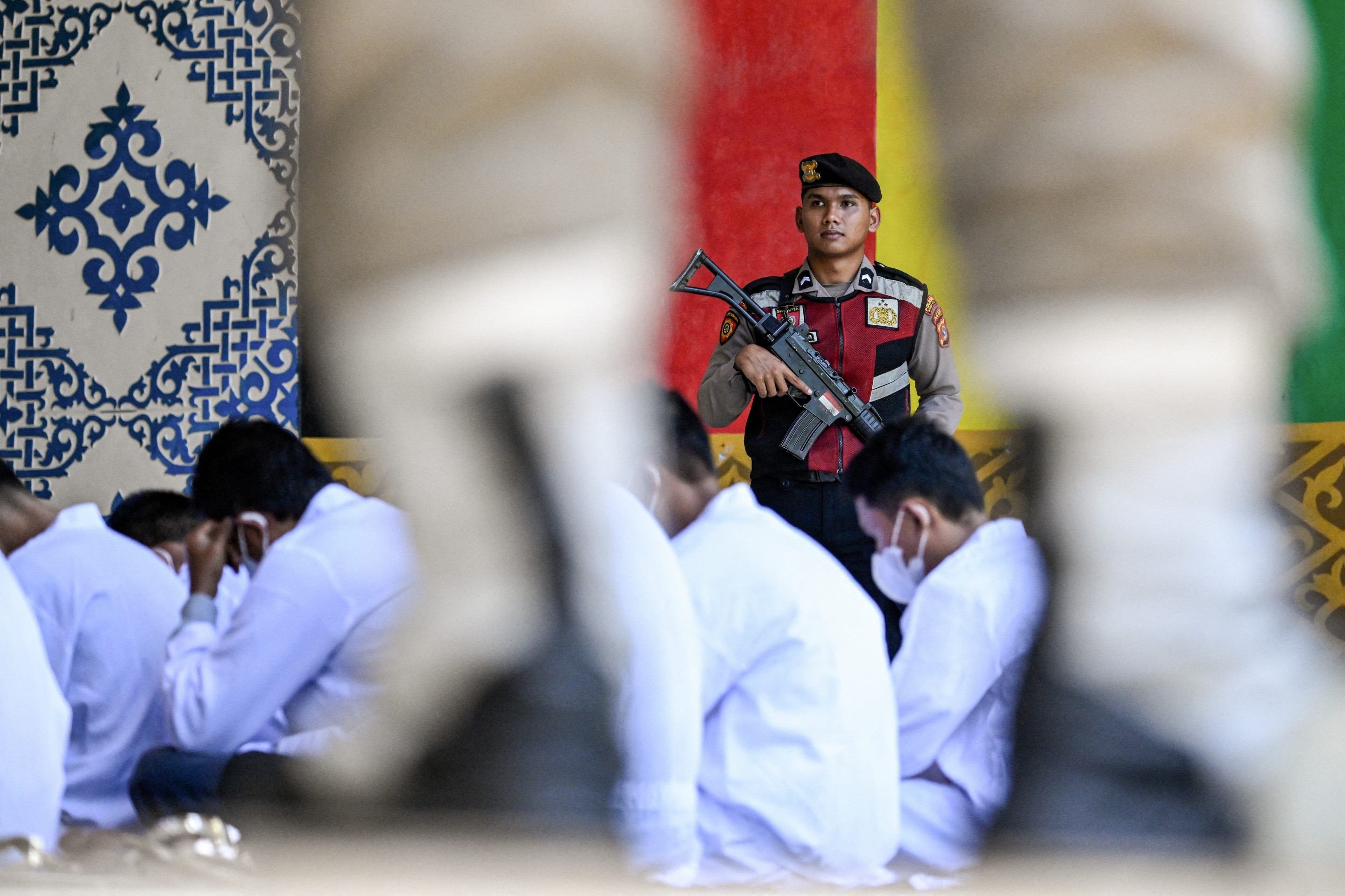 Um policial observa homens que aguardam para receber um açoite público de membros da polícia da Sharia em Banda Aceh, em 26 de agosto de 2025      