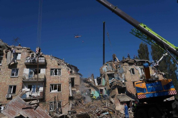 Um helicóptero de combate a incêndios sobrevoa um prédio residencial fortemente danificado, após um ataque em larga escala com drones e mísseis russos a Kiev em 28 de agosto de 2025 -  (crédito: OLEKSII FILIPPOV/AFP)