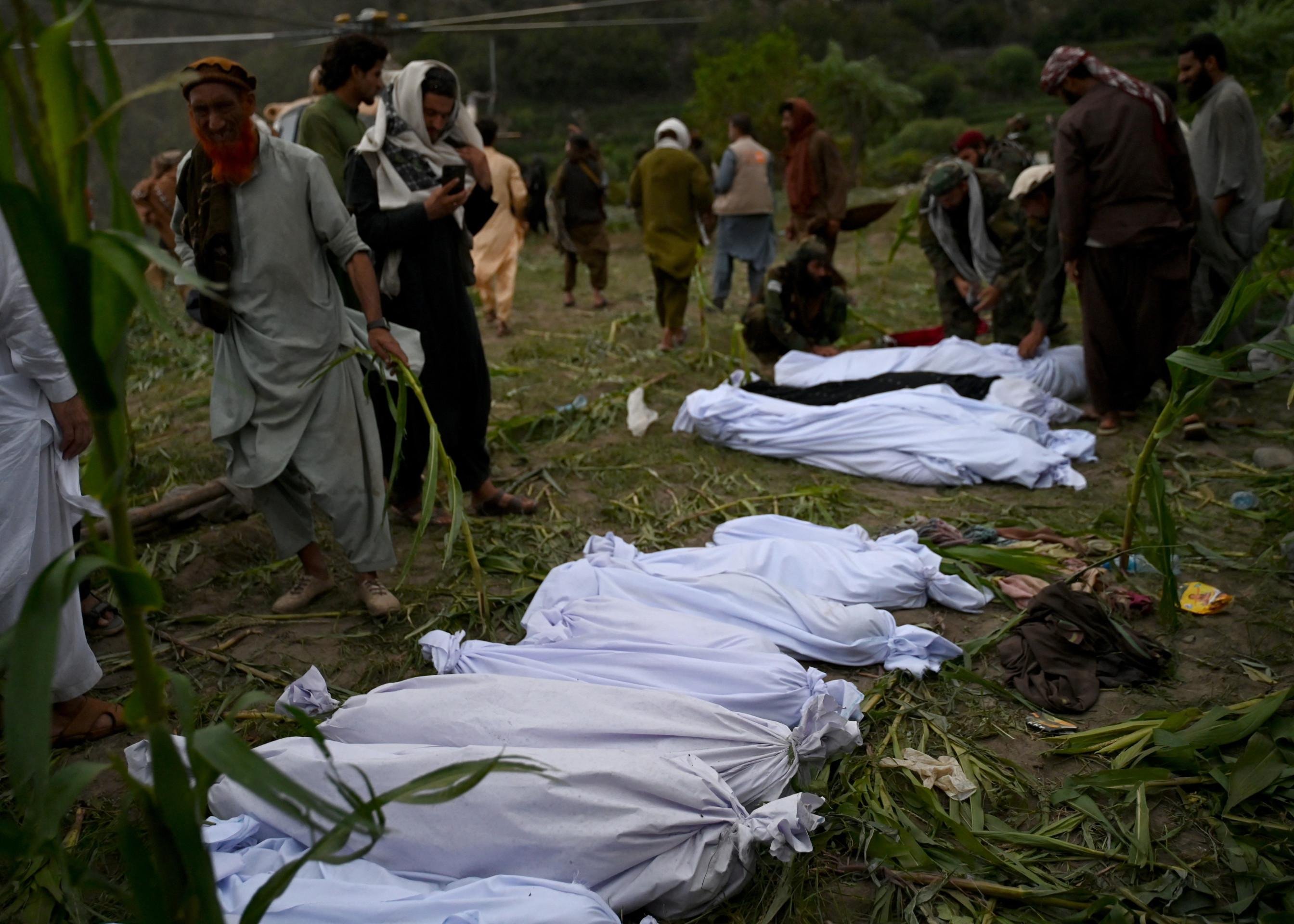 Afegãos diante de corpos das vítimas envoltos em mortalhas, no mesmo vilarejo 