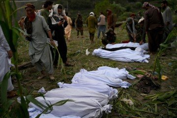 Afegãos diante de corpos das vítimas envoltos em mortalhas, no mesmo vilarejo 