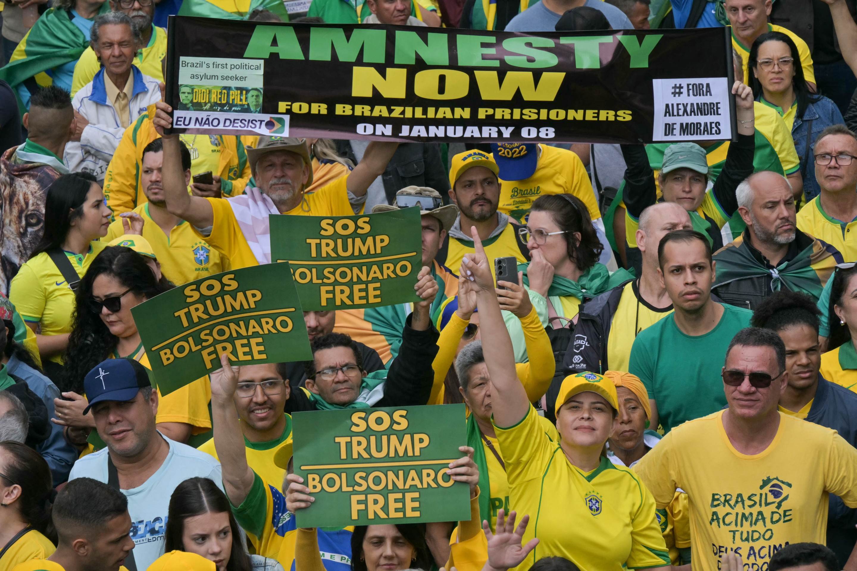 Apoiadores do ex-presidente brasileiro (2019-2022) Jair Bolsonaro, em julgamento por sua suposta participação em uma tentativa de golpe, seguram faixas com os dizeres 