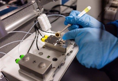 Cientista manipula o pequeno chip circular, que será utilizado no dispositivo final e funcionará como uma espécie de 