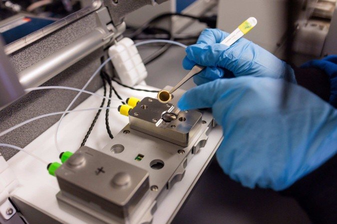 Cientista manipula o pequeno chip circular, que será utilizado no dispositivo final e funcionará como uma espécie de  Cientista manipula o pequeno chip circular, que será utilizado no dispositivo final e funcionará como uma espécie de