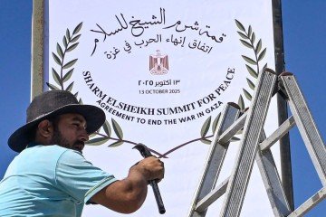 Funcionário egípcio arruma placa em Sharm el-Seikh, na véspera da Cúpula pela Paz, que reunirá líderes mundiais para assinatura do acordo de paz - (crédito: AFP) Funcionário egípcio arruma placa em Sharm el-Seikh, na véspera da Cúpula pela Paz, que reunirá líderes mundiais para assinatura do acordo de paz - (crédito: AFP)