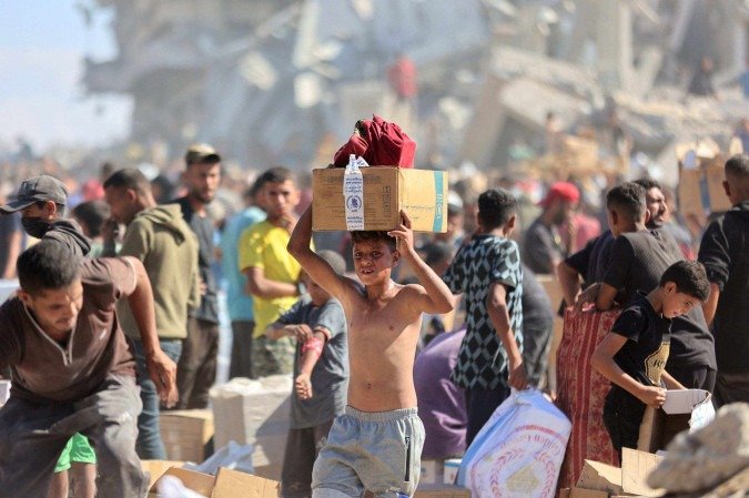 Palestinos recebem pacotes de ajuda humanitária após caminhões de ajuda humanitária entrarem pela passagem de Karem Abu Salem, em Khan Yunis, no sul da Faixa de Gaza, em 12 de outubro de 2025 -  (crédito: Omar AL-QATTAA / AFP)