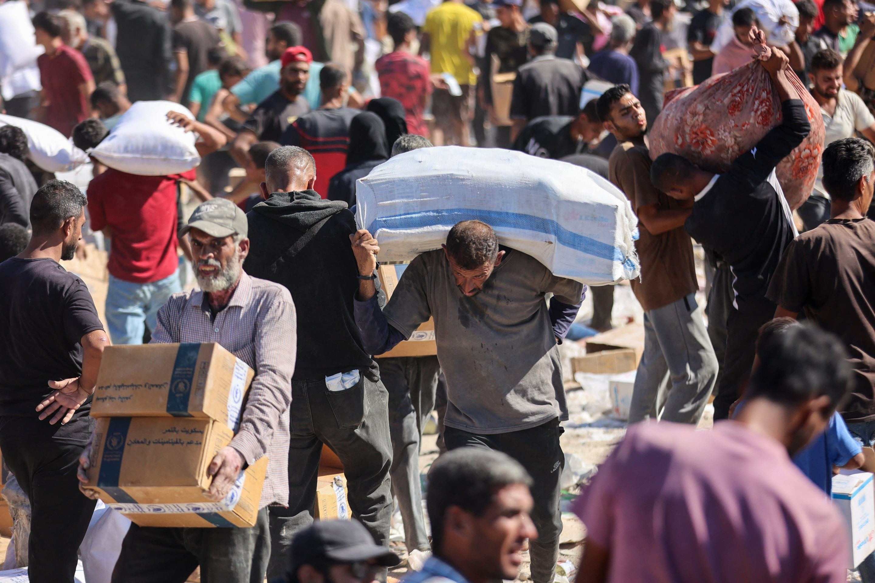 Palestinos recebem cestas básicas após a entrada de caminhões de ajuda humanitária vindos da passagem de Karem Abu Salem, em Khan Yunis, no sul da Faixa de Gaza, em 12 de outubro de 2025      
