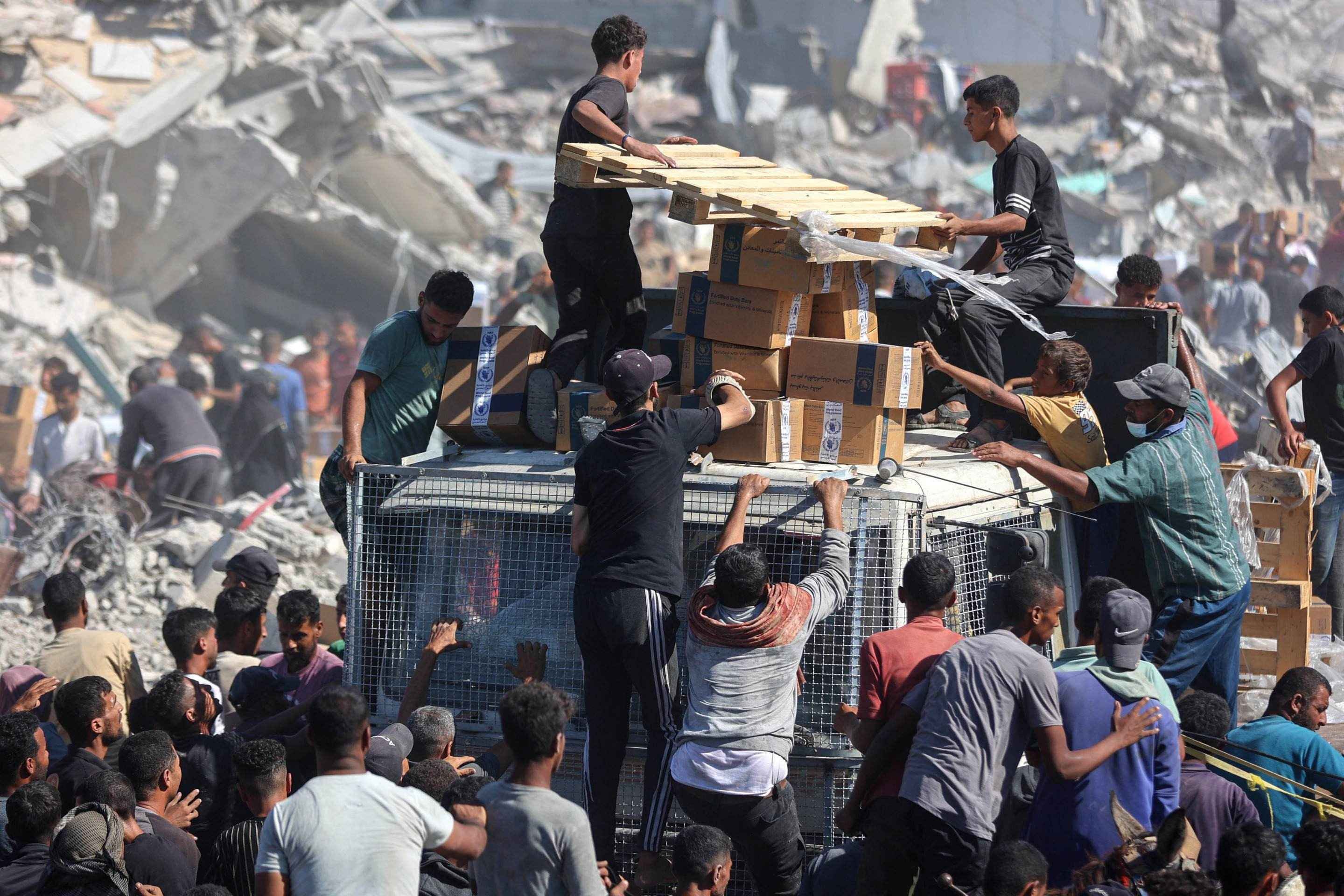 Palestinos se reúnem em torno de caminhões de ajuda humanitária que entraram pela passagem de Karem Abu Salem, em Khan Yunis, no sul da Faixa de Gaza, em 12 de outubro de 2025      