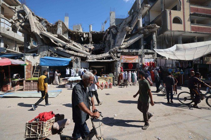 Palestinos caminham diante de pédio destruído, em mercado improvisado, no campo de refugiados de Nuseirat, no centro da Faixa de Gaza - (crédito: Eyad Baba/AFP) Palestinos caminham diante de pédio destruído, em mercado improvisado, no campo de refugiados de Nuseirat, no centro da Faixa de Gaza - (crédito: Eyad Baba/AFP)