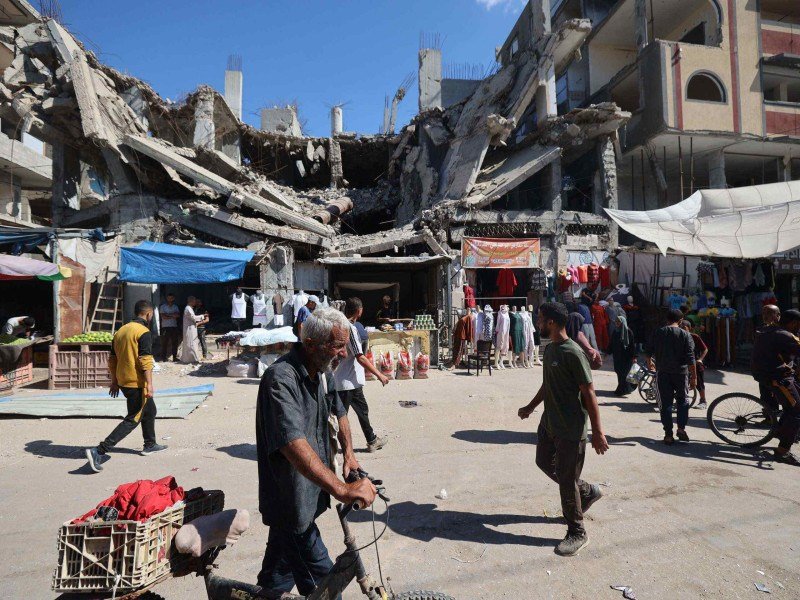 Palestinos caminham diante de pédio destruído, em mercado improvisado, no campo de refugiados de Nuseirat, no centro da Faixa de Gaza  -  (crédito: Eyad Baba/AFP)