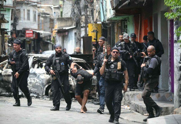 Policiais levam suspeito detido na Operação Contenção: segundo o governo do Rio de Janeiro, a ação foi deflagrada 'após mais de um ano de investigação e 60 dias de planejamento' -  (crédito: Mauro Pimentel/AFP       )