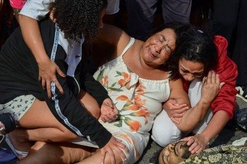  EDITORS NOTE: Graphic content / Women weep next to a dead man lying among a line of bodies on Sao Lucas Square of the Vila Cruzeiro favela at the Penha complex in Rio de Janeiro, Brazil, on October 29, 2025, in the aftermath of Operacao Contencao (Operation Containment). Residents of a favela in Rio de Janeiro lined up more than 50 bodies at a plaza in their low-income neighborhood on Ocotber 29, a day after the bloodiest police operation in the city's history, AFP reported. (Photo by Pablo PORCIUNCULA / AFP)       