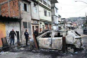 Policiais estão ao lado de um carro incendiado que fazia parte de uma barricada montada durante a Operação Contenção na favela Vila Cruzeiro, no complexo da Penha, no Rio de Janeiro, Brasil, em 28 de outubro de 2025 - (crédito: MAURO PIMENTEL / AFP) Policiais estão ao lado de um carro incendiado que fazia parte de uma barricada montada durante a Operação Contenção na favela Vila Cruzeiro, no complexo da Penha, no Rio de Janeiro, Brasil, em 28 de outubro de 2025 - (crédito: MAURO PIMENTEL / AFP)