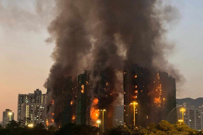  Thick smoke and flames rise as a major fire engulfs several apartment blocks at Wang Fuk Court in Hong Kong's Tai Po district on November 26, 2025. Four people died after multiple blocks in a Hong Kong residential estate went up in flames on November 26, with local media earlier reporting that some residents were trapped. (Photo by Yan ZHAO / AFP)
       -  (crédito: Yan ZHAO / AFP)