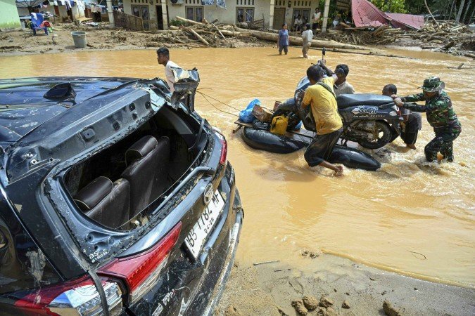  Villagers push a motorcycle on a makeshift raft along an inundated road in the aftermath of flash floods at Tukka village, Central Tapanuli, North Sumatra province, on December 2, 2025. The death toll from floods and landslides that have struck Indonesia's Sumatra island since last week has risen to 712, the National Disaster Management Agency said on December 2. (Photo by YT HARIONO / AFP)
      Caption 