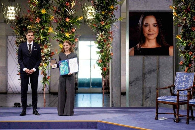 Ana Corina Sosa (D), filha de María Corina Machado, exibe a medalha e o diploma do Nobel da Paz, em solenidade na capital da Noruega
- (crédito: Ole Berg-Rusten/NTB/AFP) Ana Corina Sosa (D), filha de María Corina Machado, exibe a medalha e o diploma do Nobel da Paz, em solenidade na capital da Noruega
- (crédito: Ole Berg-Rusten/NTB/AFP)