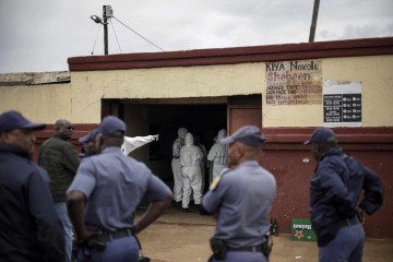  Agentes do Serviço de Polícia da África do Sul (SAPS) observam membros do Serviço de Patologia Forense do SAPS trabalhando no local de um ataque a uma taverna em Bekkersdal, em 21 de dezembro de 2025 -  (crédito: AFP)