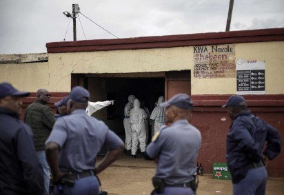  Agentes do Serviço de Polícia da África do Sul (SAPS) observam membros do Serviço de Patologia Forense do SAPS trabalhando no local de um ataque a uma taverna em Bekkersdal, em 21 de dezembro de 2025 -  (crédito: AFP)