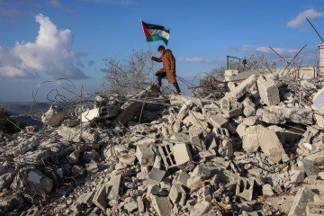Garoto segura a bandeira palestina sobre ruínas de casa demolida por Israel, em Bazzaryah, na Cisjordânia  -  (crédito: Zain Jaafar/AFP)