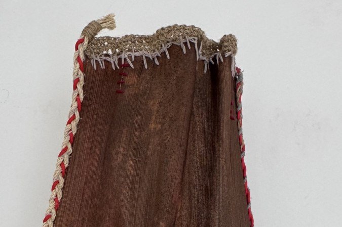 Um caule de coqueiro se mistura a papel de algodão, folhas, tinta e fio de lã nesse objeto