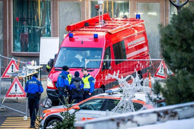  Police officers and rescuers stand next to a firefighters vehicle on the site of a fire that ripped through the bar Le Constellation in Crans-Montana on January 1, 2026. Several dozen people are presumed dead and around 100 injured after a fire ripped through a crowded bar in the luxury Swiss ski resort of Crans-Montana, Swiss police said on January 1, 2026. Police, firefighters and rescuers rushed to the popular resort, which is set to host the Ski World Cup from January 30, after the fire broke out in the early hours of New Year's Day. (Photo by MAXIME SCHMID / AFP)
       -  (crédito:  MAXIME SCHMID / AFP)