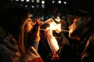 Manifestantes acendem cigarro em imagem em chamas do aiatolá Ali Khamenei  -  (crédito: Carlos Jasso/AFP)
