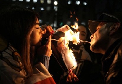 Manifestantes acendem cigarro em imagem em chamas do aiatolá Ali Khamenei  -  (crédito: Carlos Jasso/AFP) -Manifestantes acendem cigarro em imagem em chamas do aiatolá Ali Khamenei  -  (crédito: Carlos Jasso/AFP)