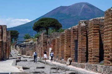 Visitantes caminham pelo sítio arqueológico, aos pés do vulcão Vesúvio (ao fundo): referência da arquitetura do império -  (crédito:  Tiziana FABI/AFP)