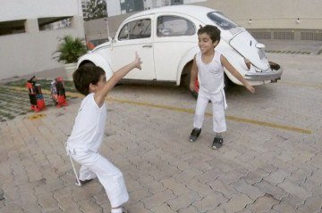 Os gêmeos Heitor e Ulisses brincam em frente ao carro do pai, Clístenes Cardoso