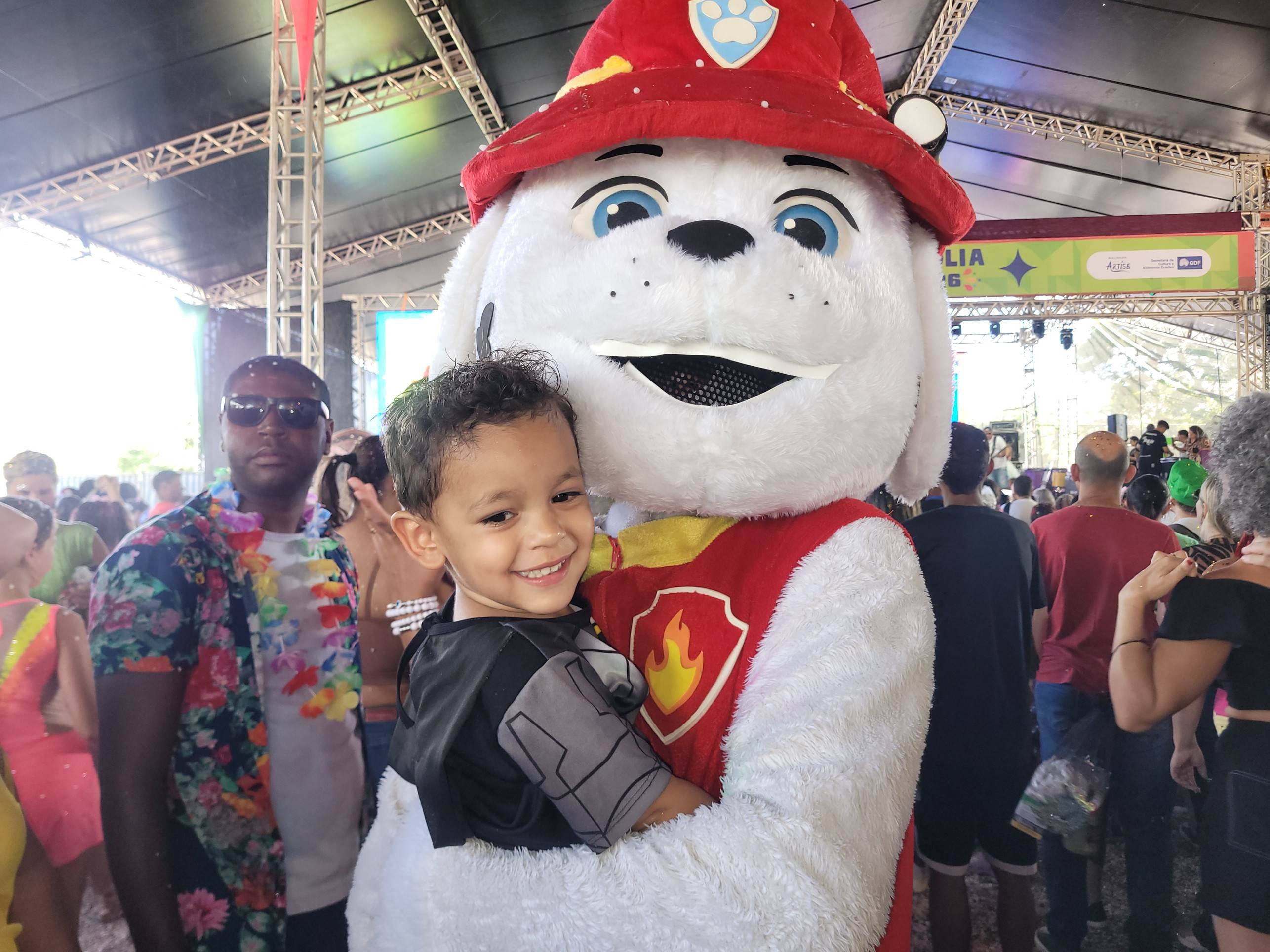 Crian&ccedil;a no colo de um rapaz vestido de um dos personagens do Patrulha Canina