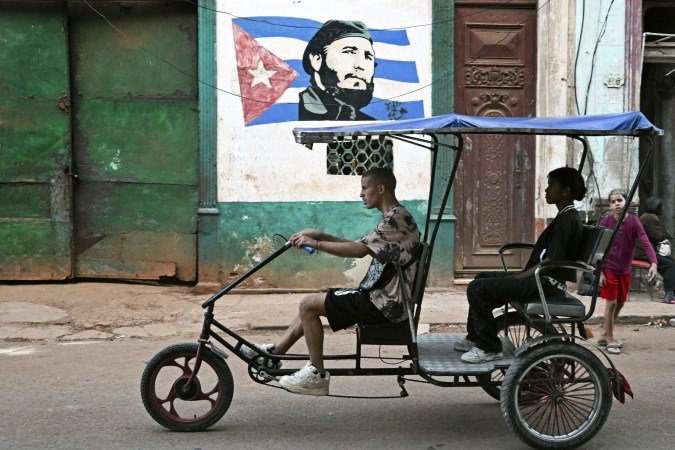 Condutor de bicitáxi leva passageira em rua de Havana, com a imagem de Fidel Castro ao fundo: alternativa à escassez de combustível 